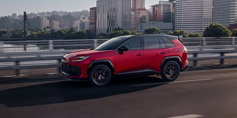 A red Toyota RAV4 Plug-in Hybrid driving on a city bridge.