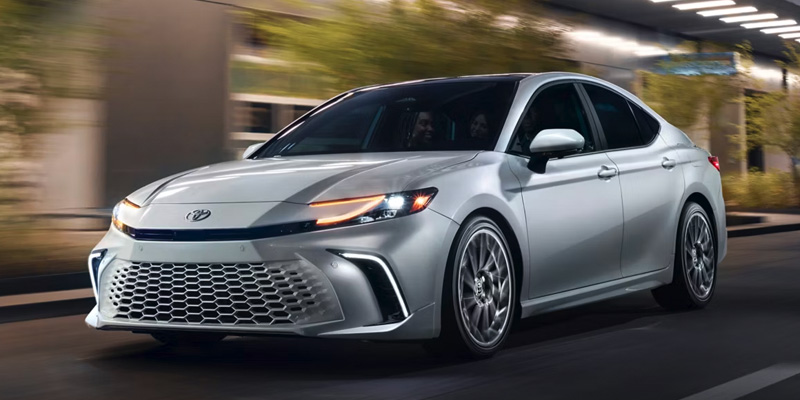 A silver Toyota Camry driving through a city at night.