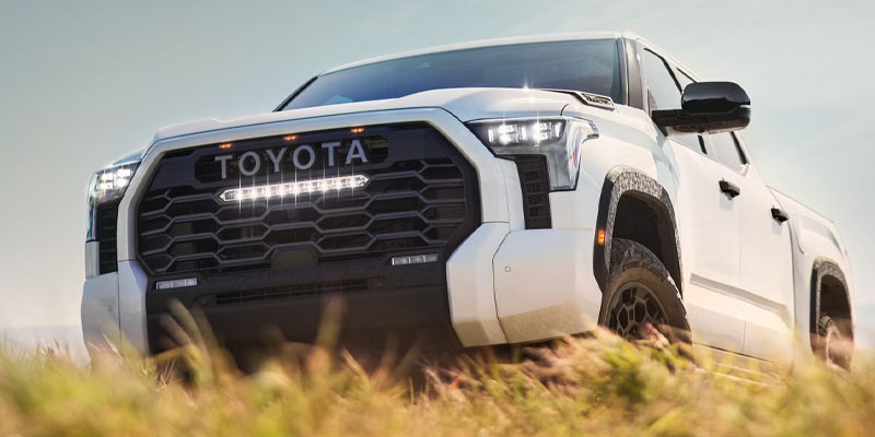 White Toyota Tundra pickup truck driving through an outdoor landscape.